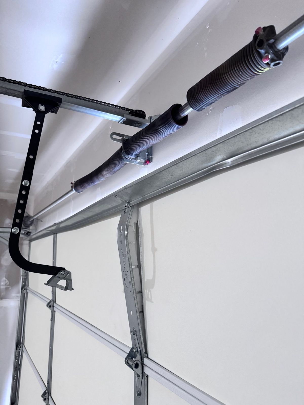 Broken garage door torsion spring on the shaft above a Coquitlam garage door, gap visible between the two halves of the snapped spring