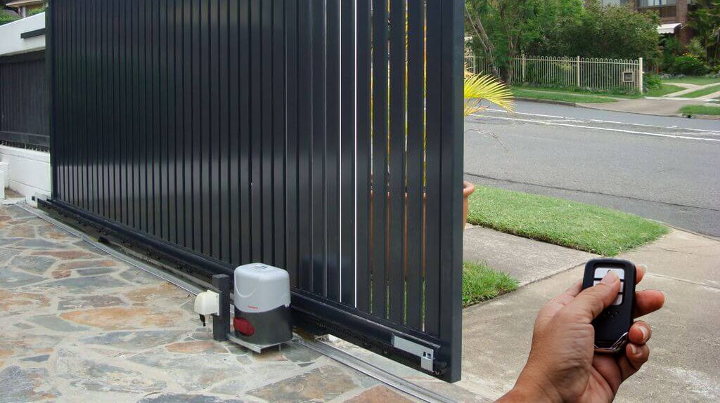 Hand holding LiftMaster remote control opening a residential sliding driveway gate in Port Coquitlam after POCO Garage Doors programmed the receiver