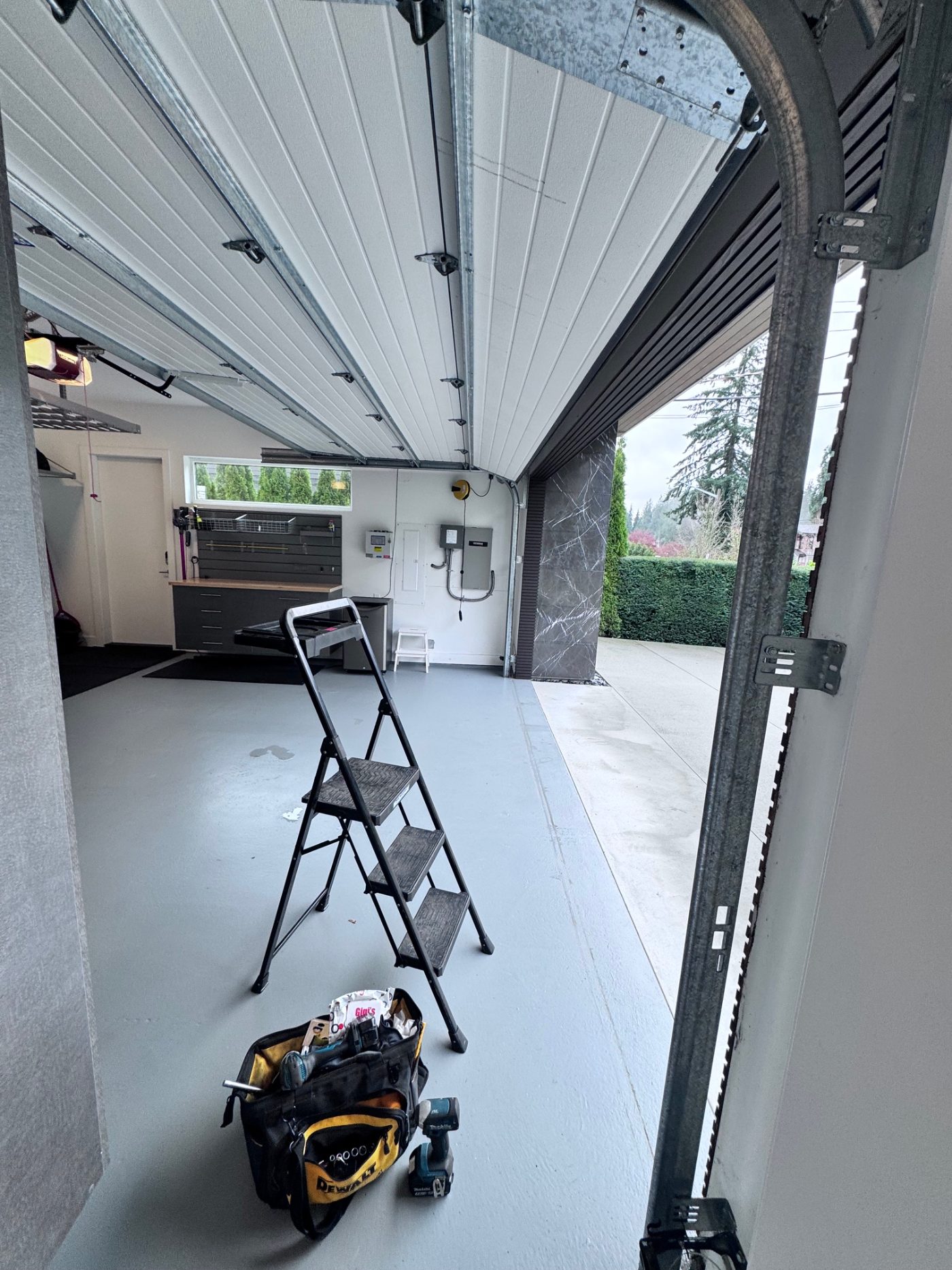 Residential garage door stuck in the open position on a Tri-Cities driveway with tools and a step ladder inside — photographed during a POCO Garage Doors same-day service call