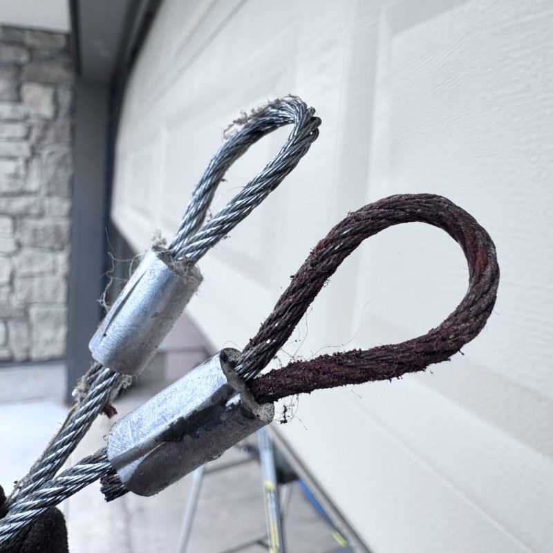 Frayed and broken garage door cable next to a new replacement cable