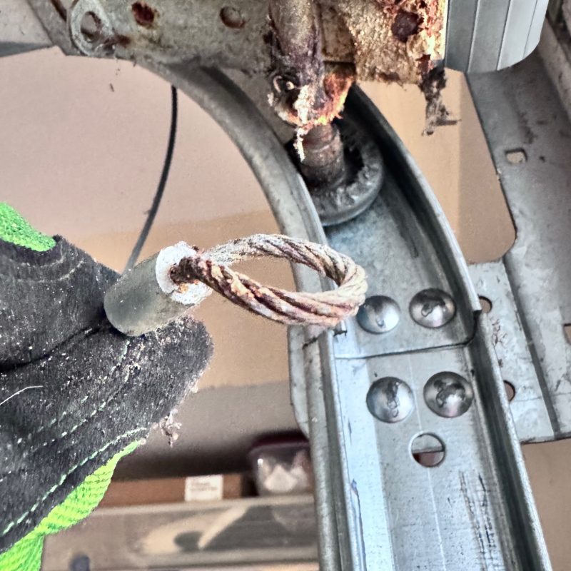 Rusted garage door cable showing internal corrosion before failure