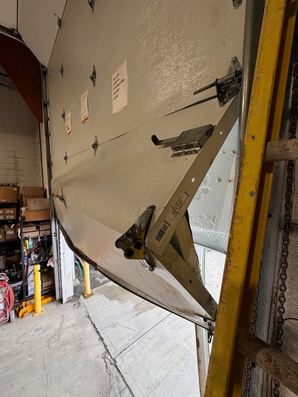 Commercial warehouse garage door with forklift-strike damage — bent bottom section and twisted track — being rebuilt by POCO Garage Doors in Coquitlam