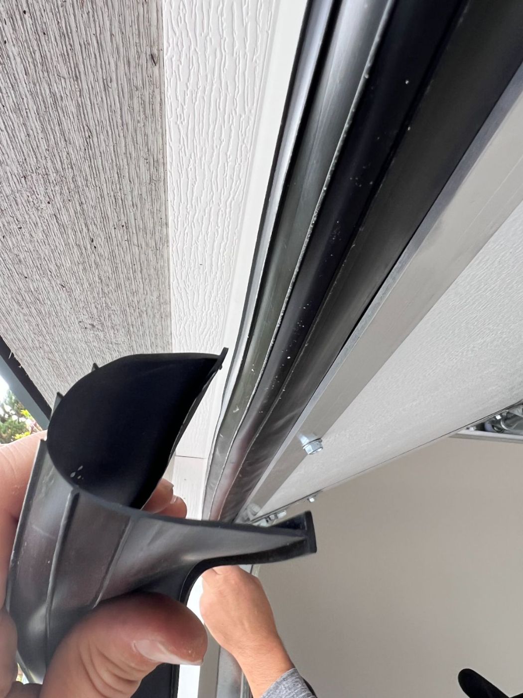 New black T-shaped rubber bottom seal being fitted into the retainer track of a Port Coquitlam garage door