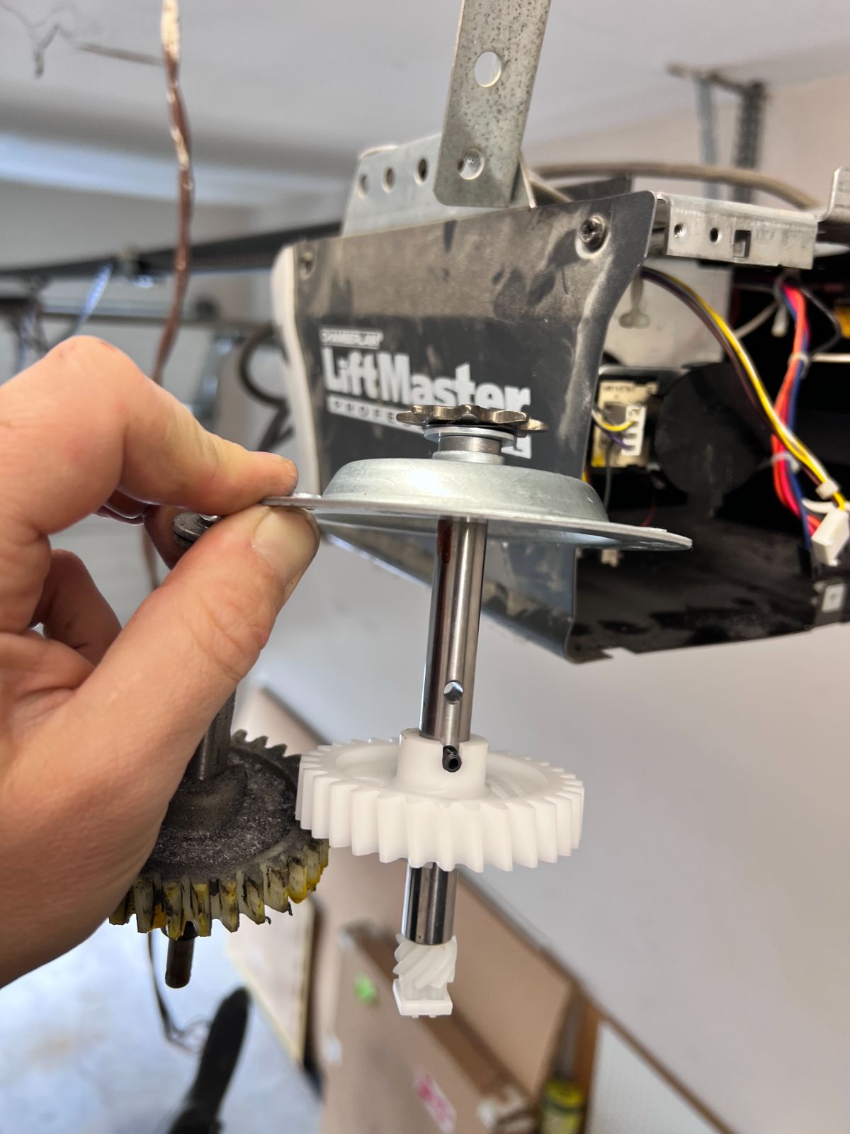 Worn brass drive gear with stripped teeth removed from a LiftMaster Professional opener in Port Coquitlam, next to new white nylon replacement gear and sprocket