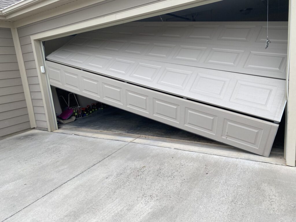 Sectional garage door dramatically off track on a Port Coquitlam driveway — bottom panel hanging out of the opening at an angle