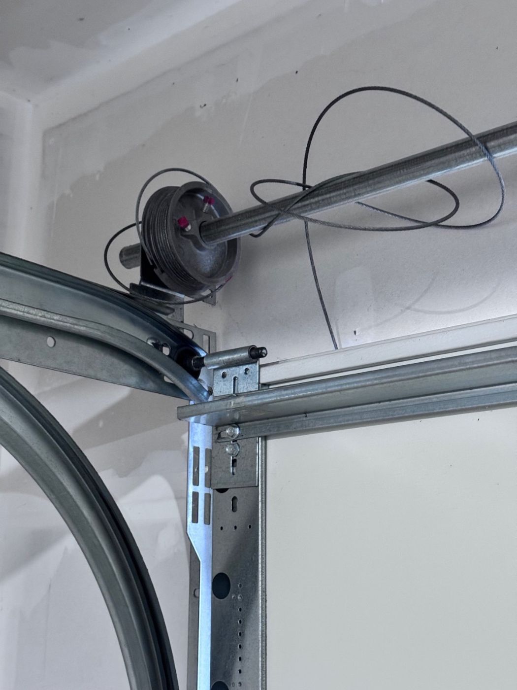 Snapped garage door cable hanging in loose loops off the cable drum at the top corner of a Port Moody garage
