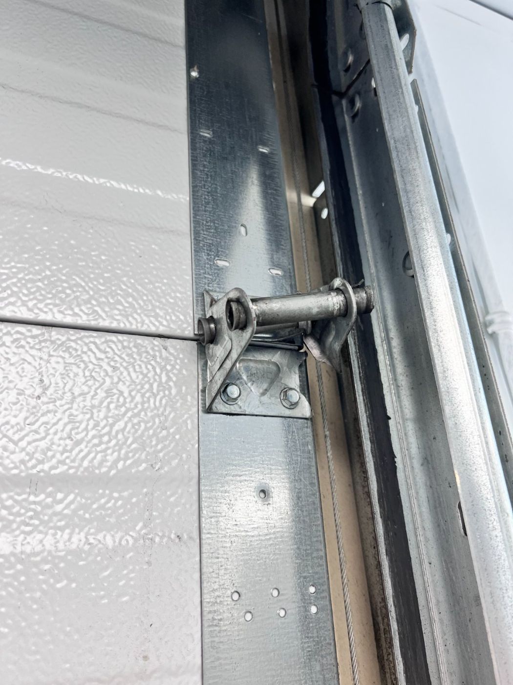 New galvanized garage door hinge and bracket installed between two white insulated panels on a Port Moody garage door