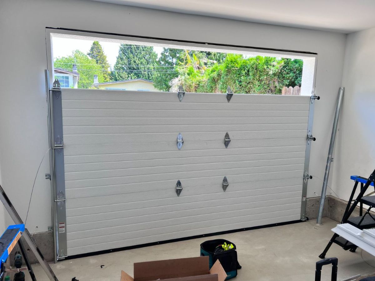 Brand new white insulated sectional garage door freshly installed inside a Port Moody garage, viewed from inside looking out