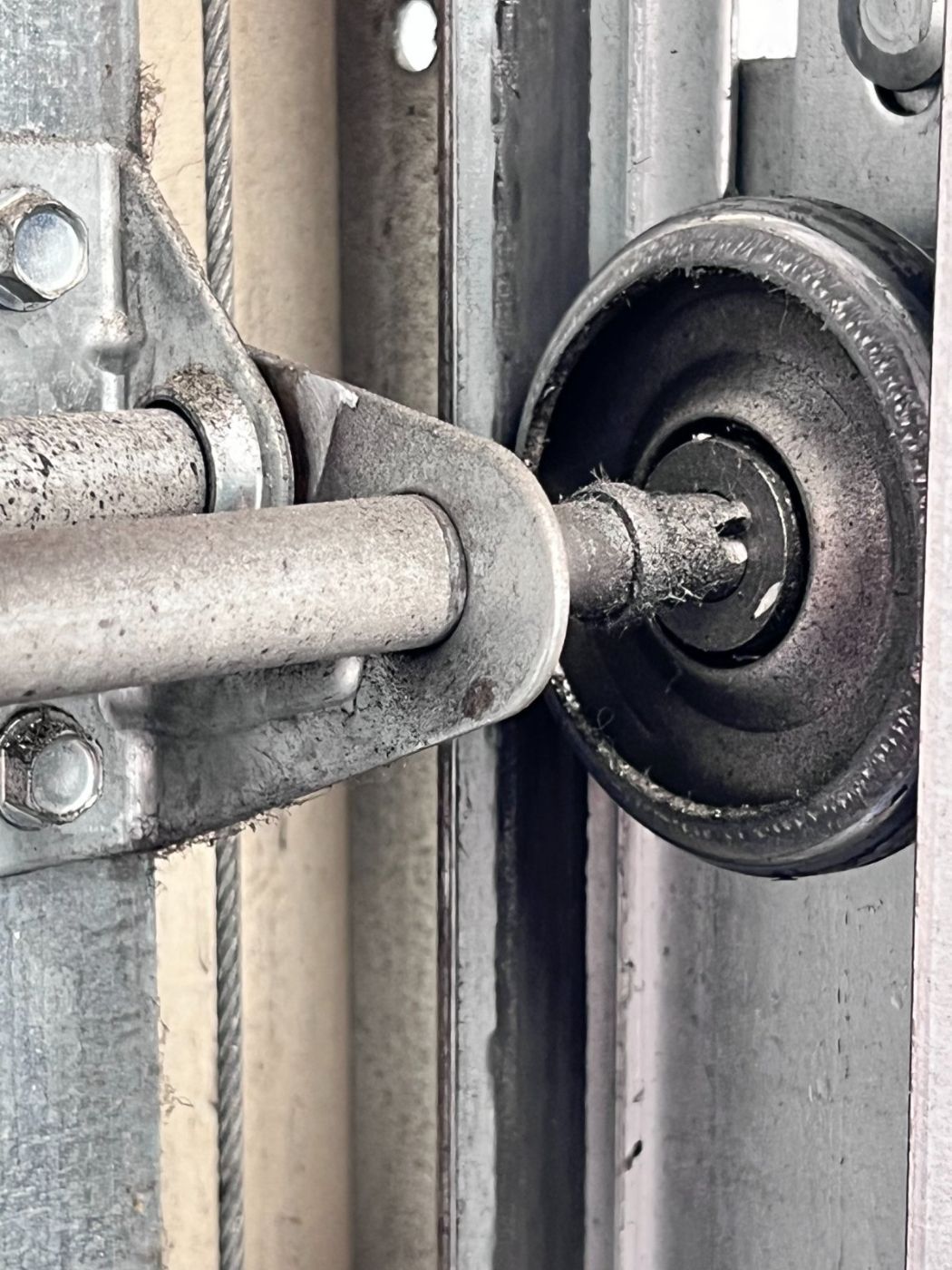 Worn black plastic garage door roller next to its mounting bracket and torsion shaft, dust and debris visible from years of use, on a Port Moody door