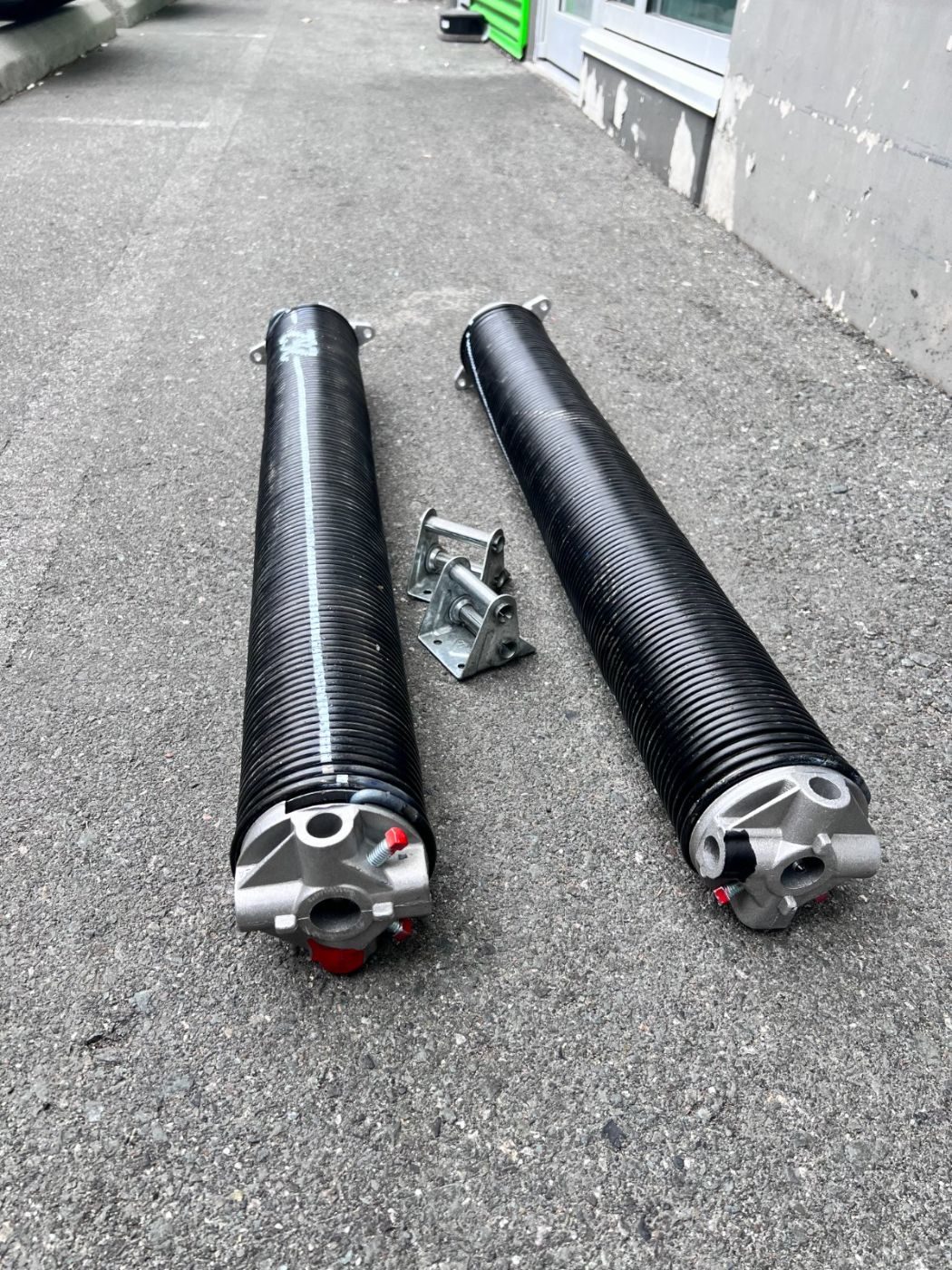 Pair of new black oil-tempered torsion springs and centre bearing plate laid out on a Port Moody driveway, ready for installation